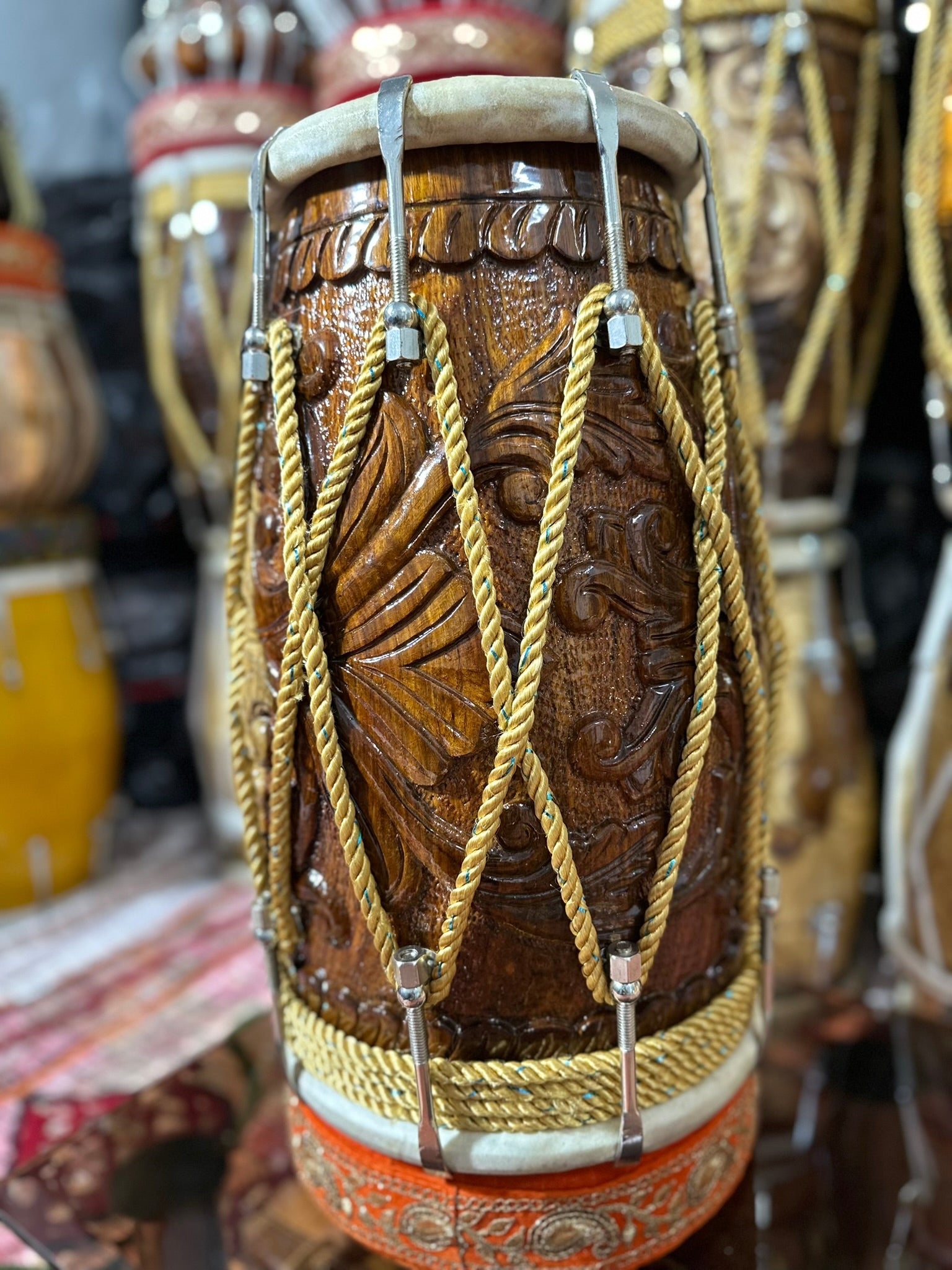 Carved wooden drum with intricate patterns and gold strings, surrounded by other drums.